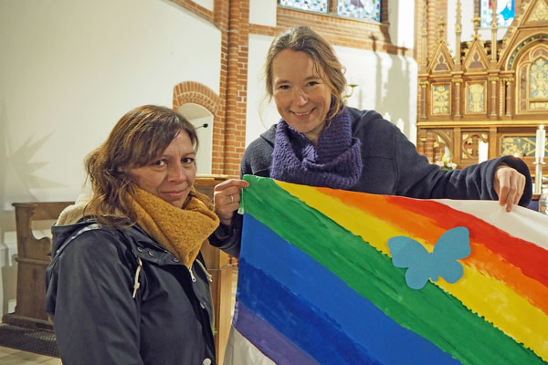 Mutter Daniela Wulff (links) und Pastorin Mareike Hansen mit dem Regenbogen-Banner, auf dem die Schmetterlinge mit den Namen der verstorbenen Kinder angebracht werden. Foto: KKLL-Annkathrin Bornholdt