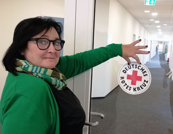 Annett Szodrzynski, Assistentin der Geschäftsführung, bringt das DRK-Logo am Eingang zur neuen Geschäftsstelle in der Schwartauer Allee an. Foto: DRK Lübeck